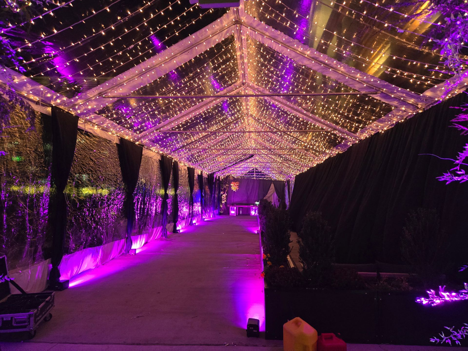 A long, clear tent with purple lights and a walkway. Sides draped in dark fabric, with a stage at the end.