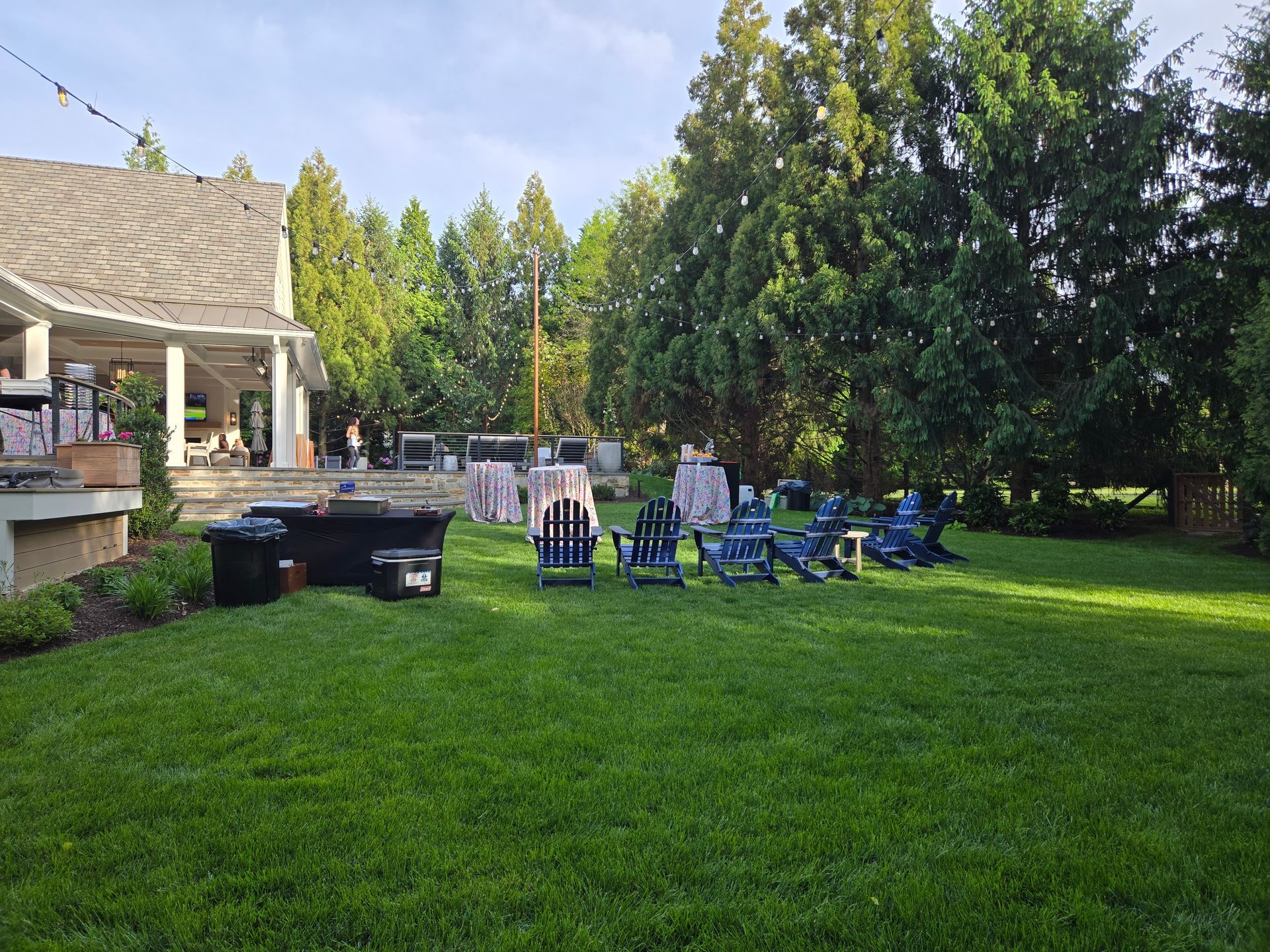 Lawn with chairs and tables set up for an outdoor event near a building and trees.