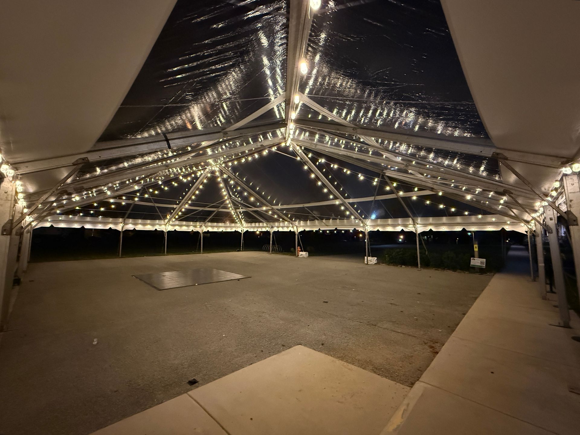Clear tent lit with string lights, set outdoors, with a dark night sky.