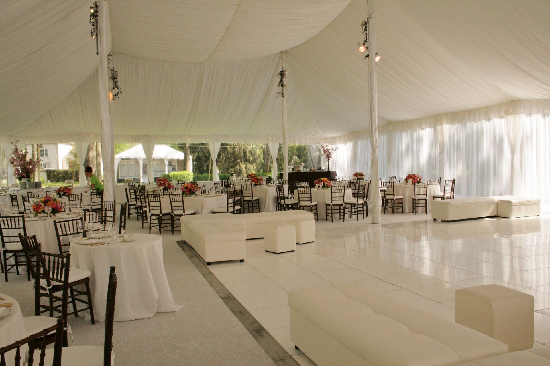 White tent interior with tables, chairs, and white seating; event setup.