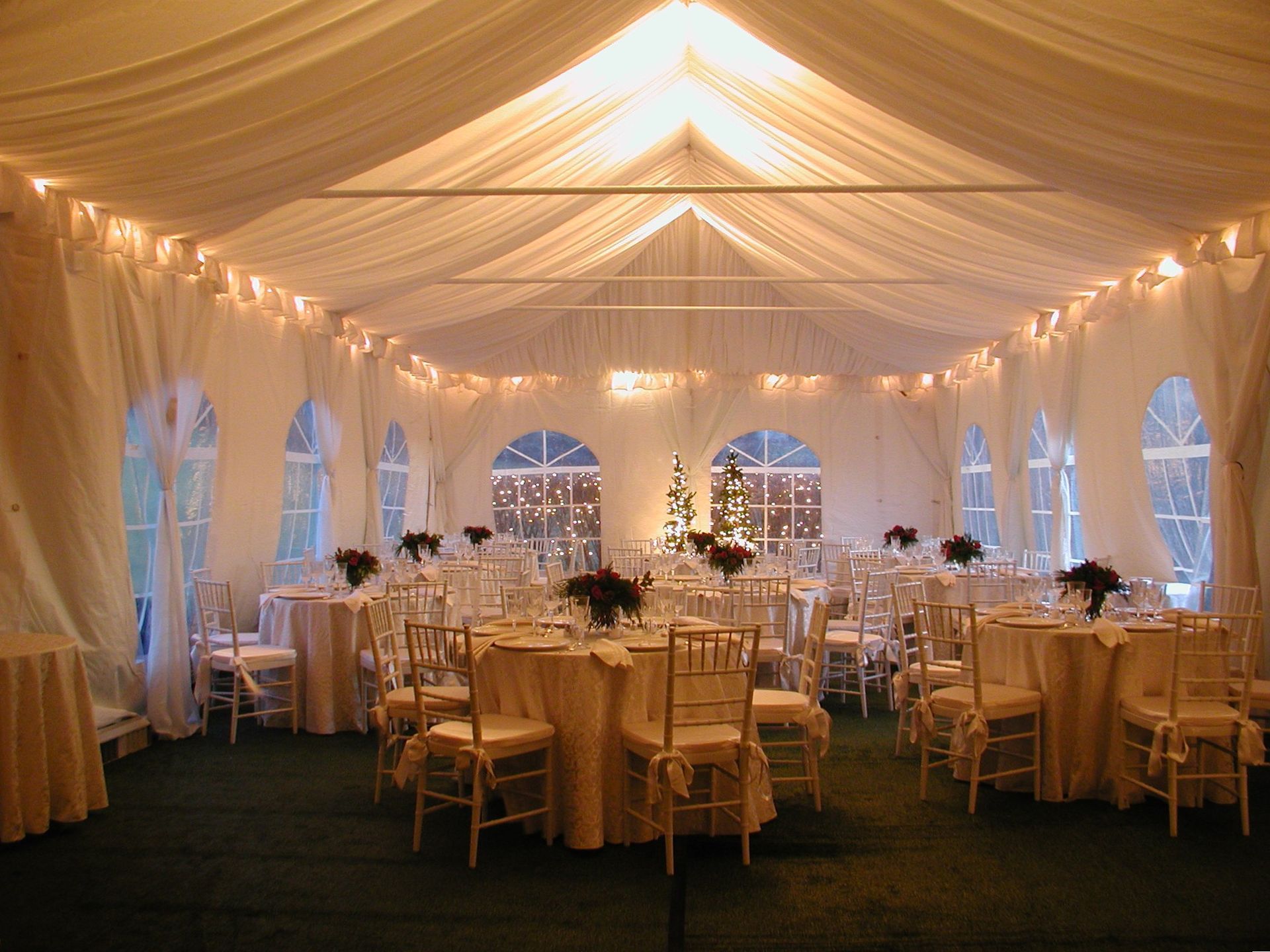 White tent interior with tables set for an event; string lights, and a Christmas tree.