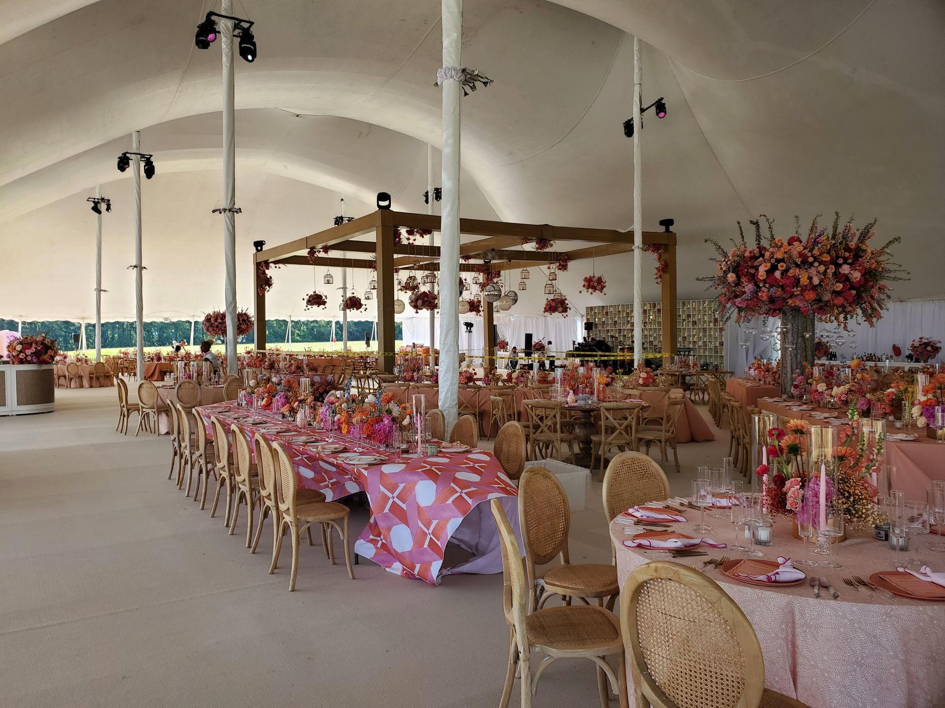 Wedding reception in a large white tent, with tables set for guests. Pink and orange floral decor.