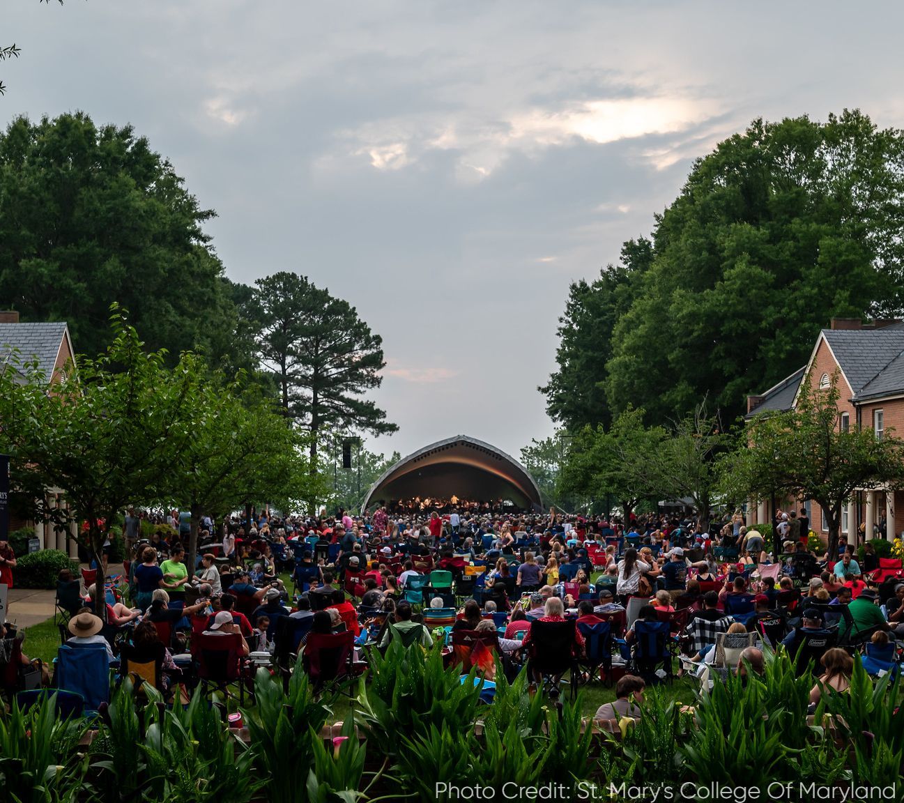 Large crowd watching a performance on an outdoor stage at St. Mary's College of Maryland, dusk.