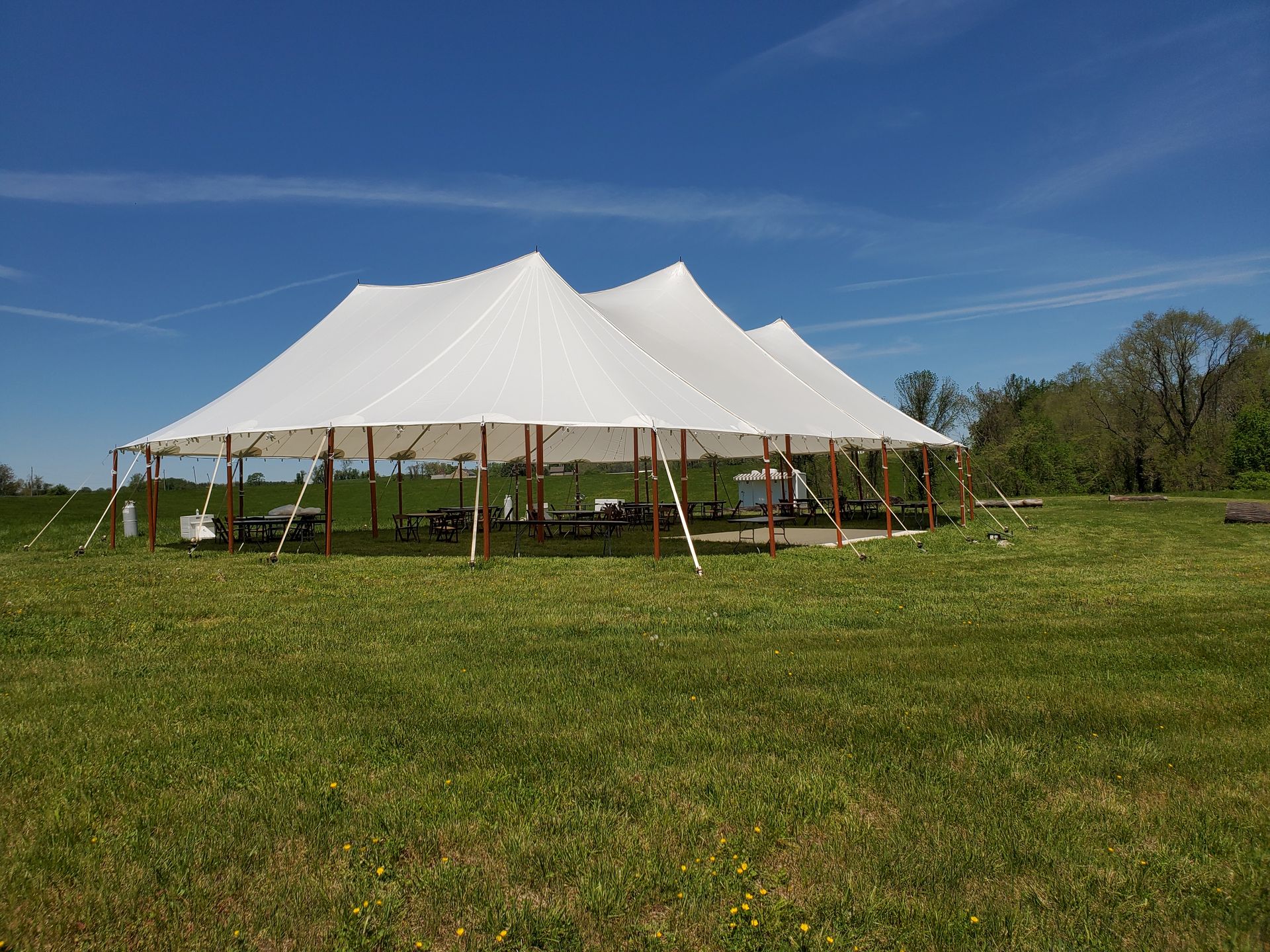 White tent set up on green grass field with blue sky.