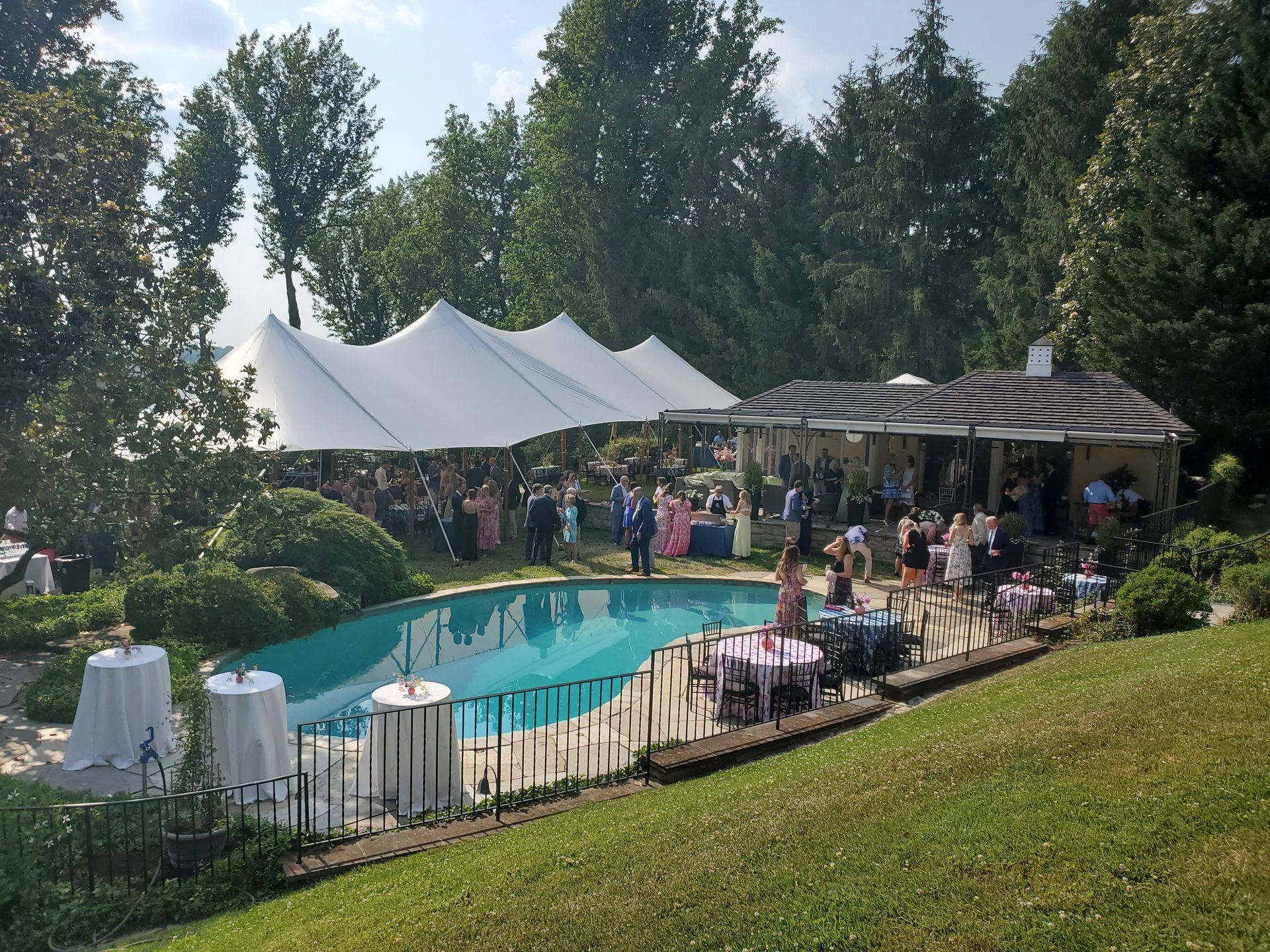 Wedding reception near a pool, tents, and outdoor patio with people socializing.