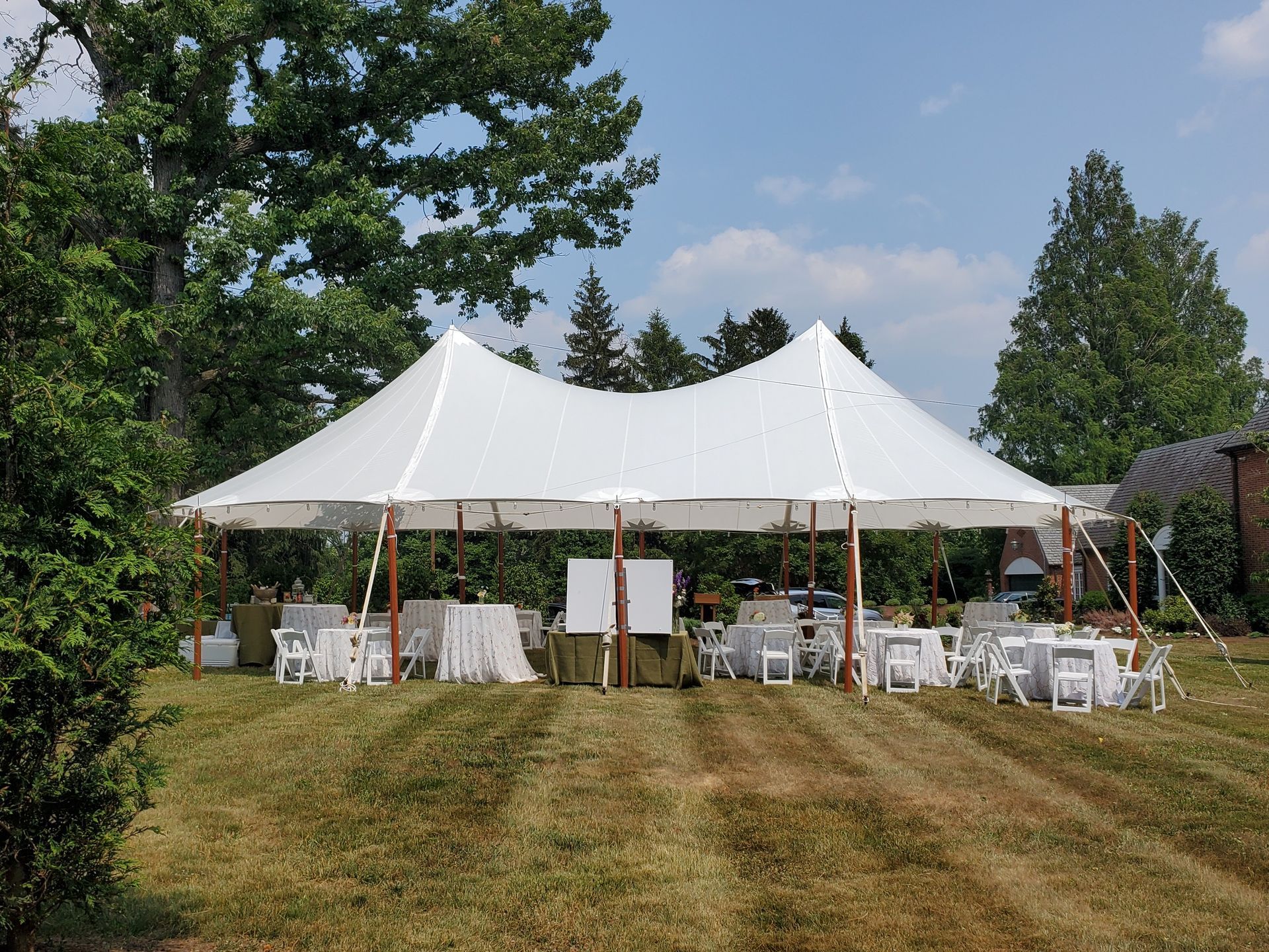 White tent set up on a grassy lawn with tables and chairs, likely for an outdoor event.