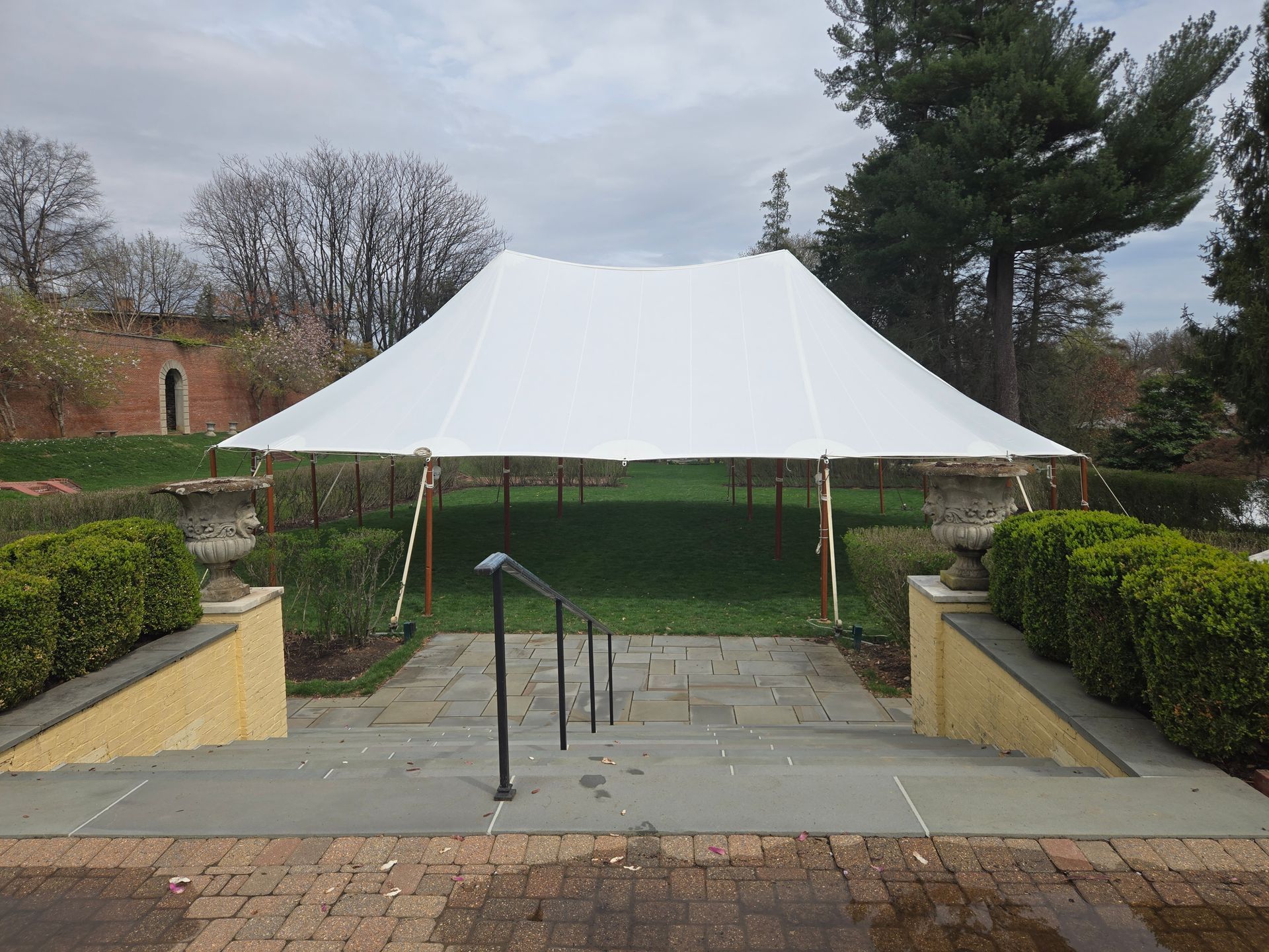 White tent set up on a green lawn, with stone steps leading up to it. Overcast sky in background.