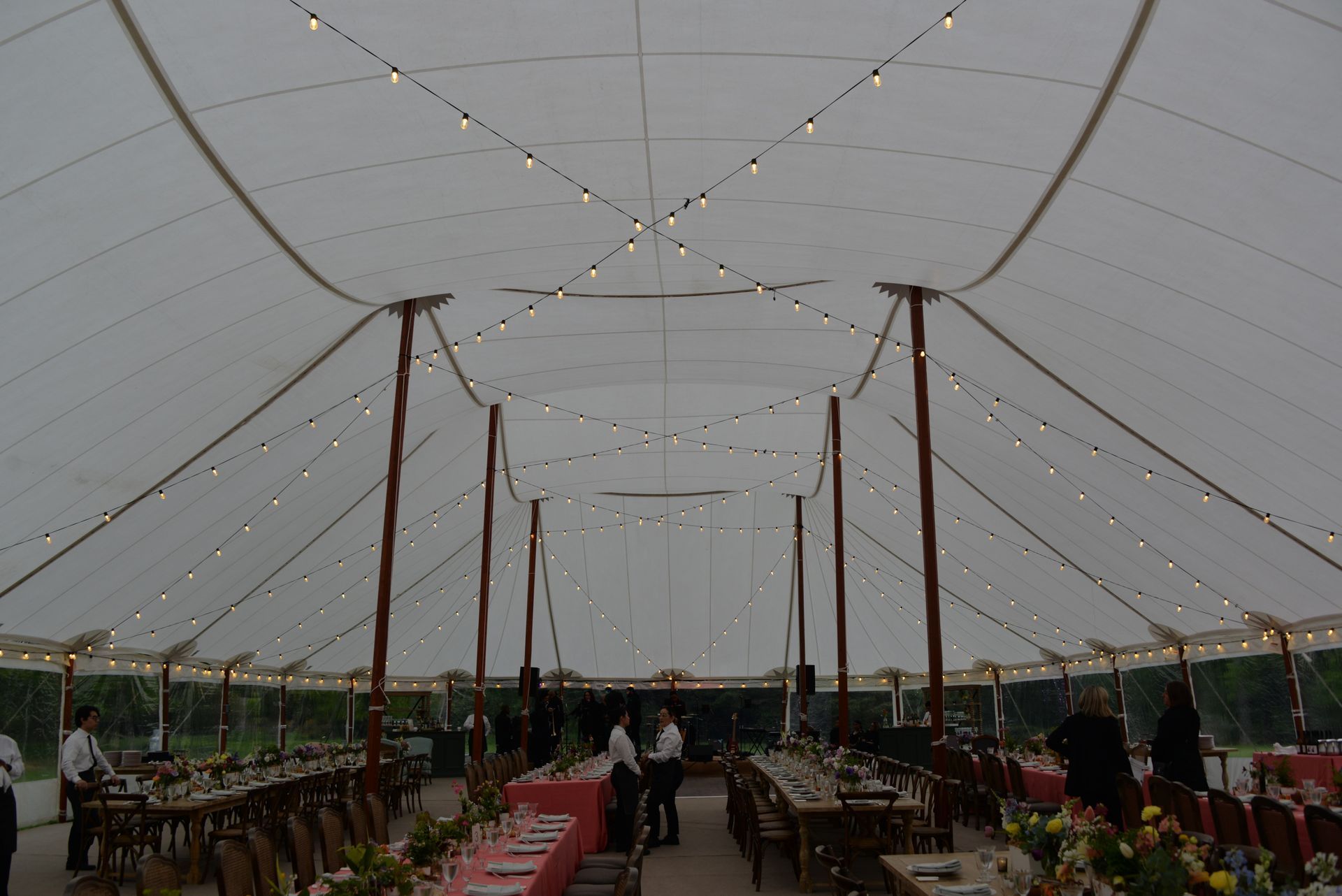 Inside view of a large white tent set for an event, tables with seating, lights hanging.