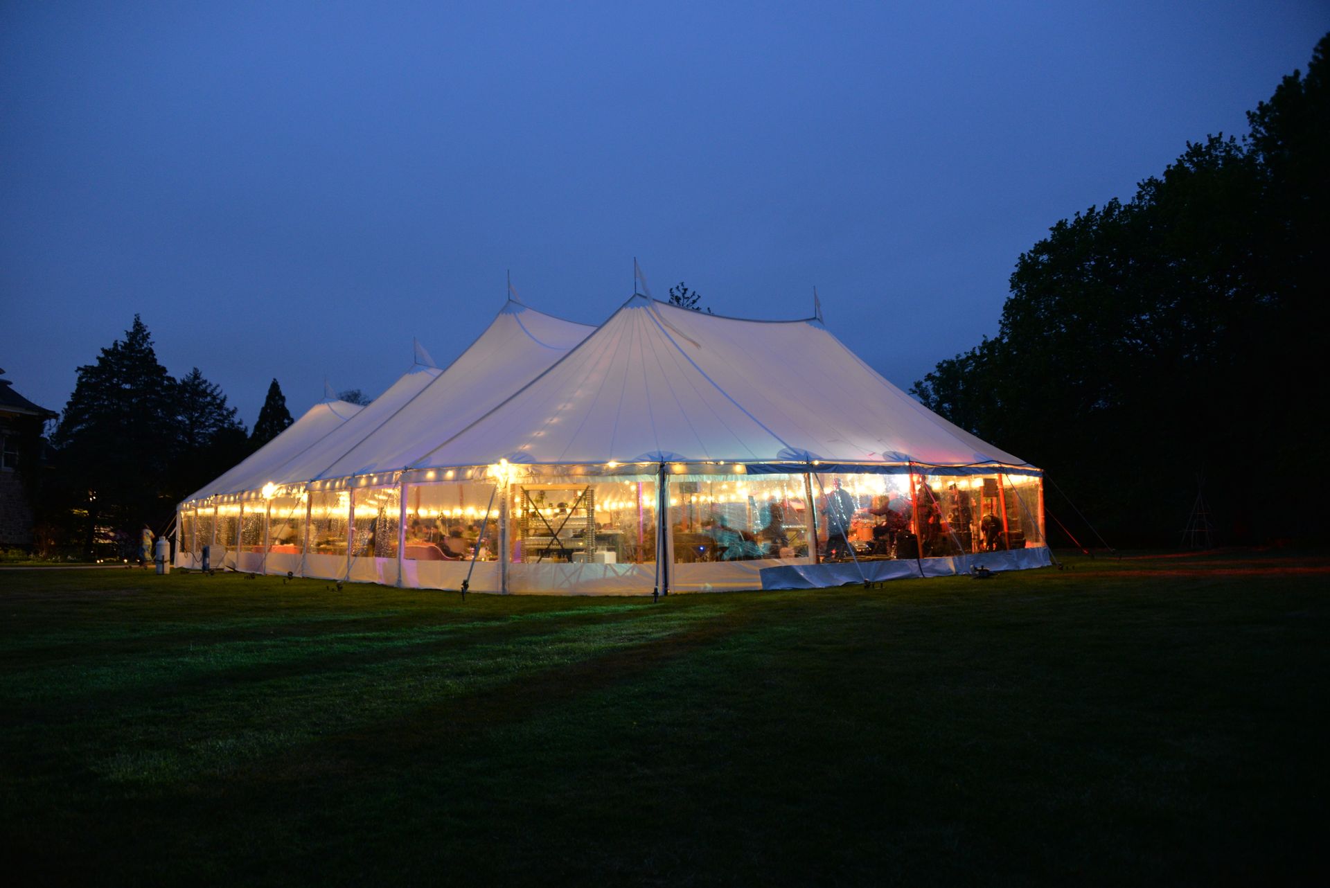 Lit event tent at night on a grassy lawn. Interior visible; warm lighting.