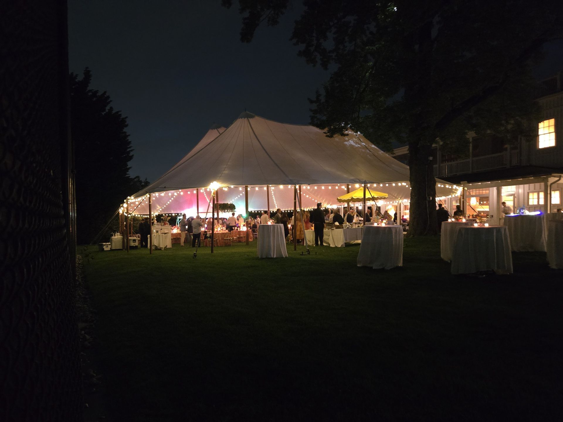 Nighttime outdoor party with a large tent and white tablecloth tables.
