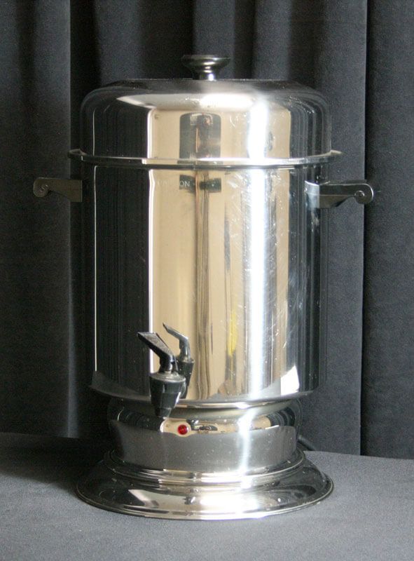 Silver coffee urn with a spigot and handles against a dark background.