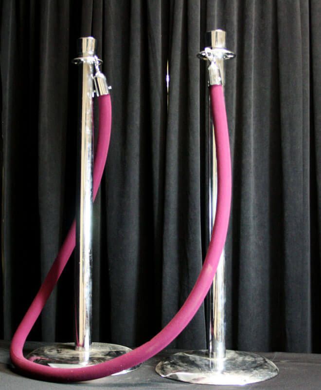Two polished chrome stanchions with a maroon velvet rope, set against a black curtain.