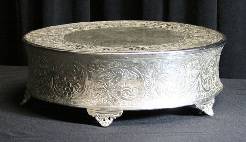 Silver, ornate cake stand on a dark surface.