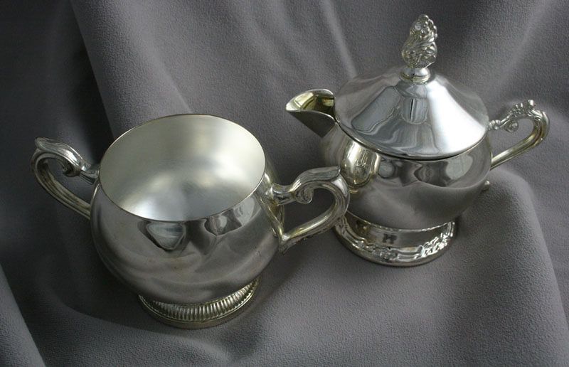 Silver sugar bowl and creamer on a gray fabric. The creamer has a lid.