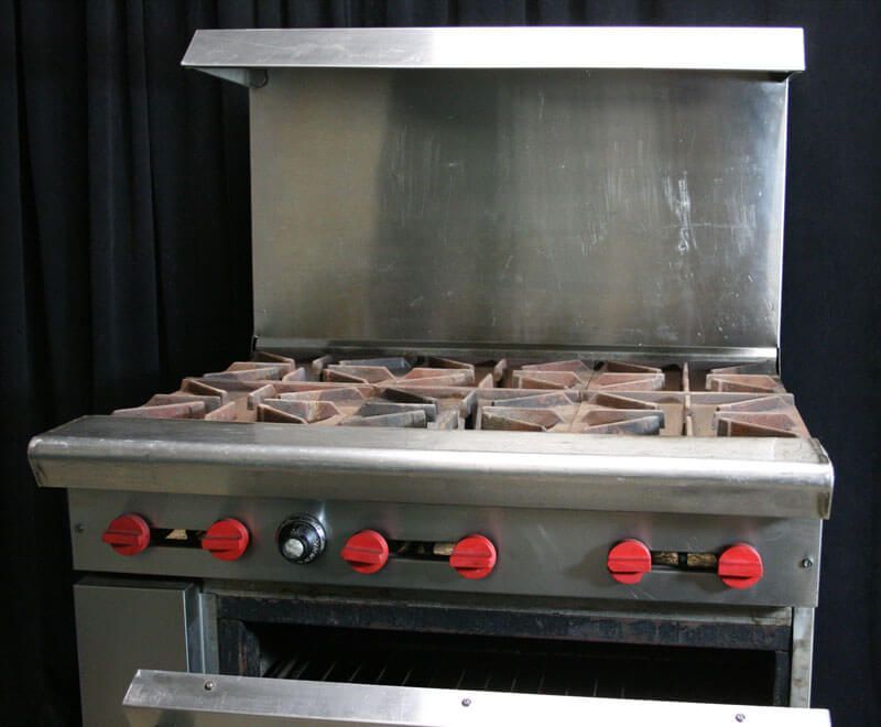 Stainless steel commercial gas range with six burners, red knobs, and oven door open.
