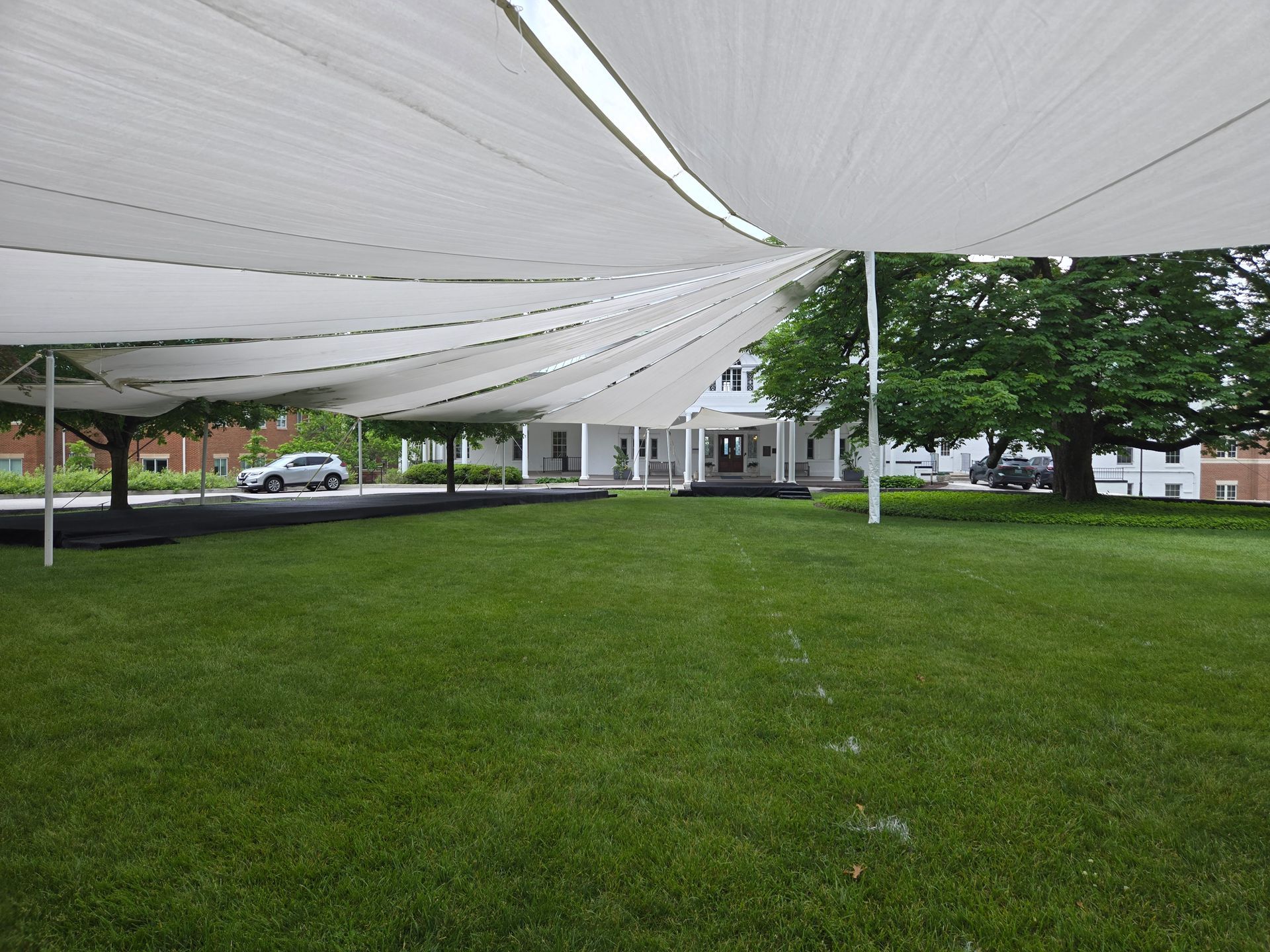 White canopies over a grassy lawn lead to a white building; a car drives in the background.