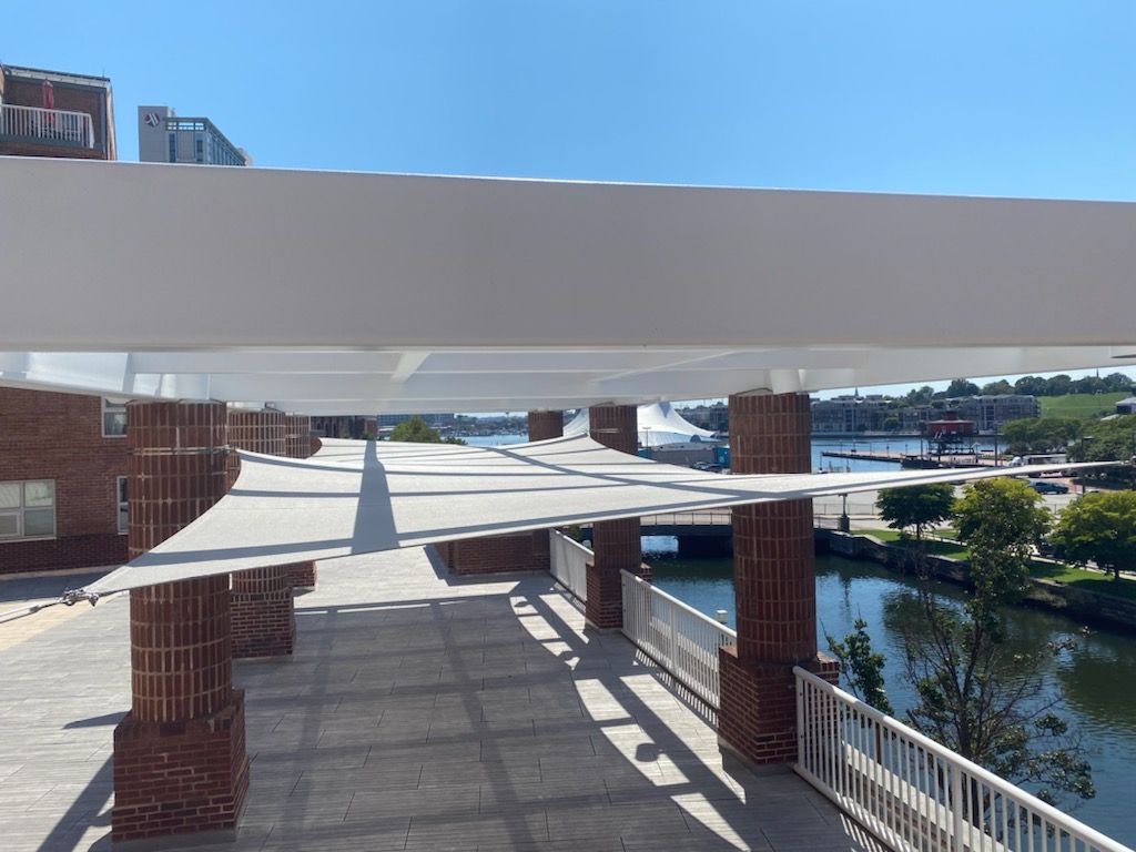 A brick and concrete walkway with shade structures overlooking a waterway on a sunny day.