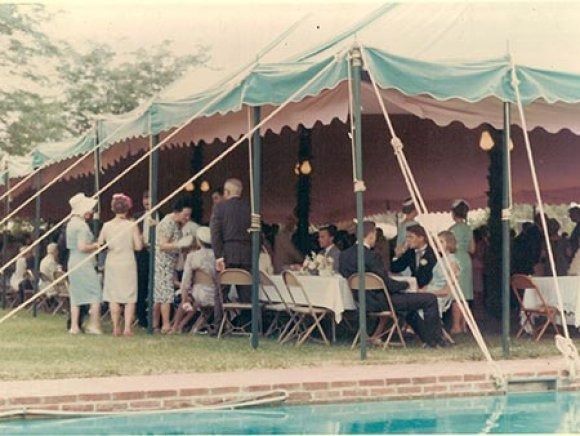 A group of people are gathered under a tent near a pool