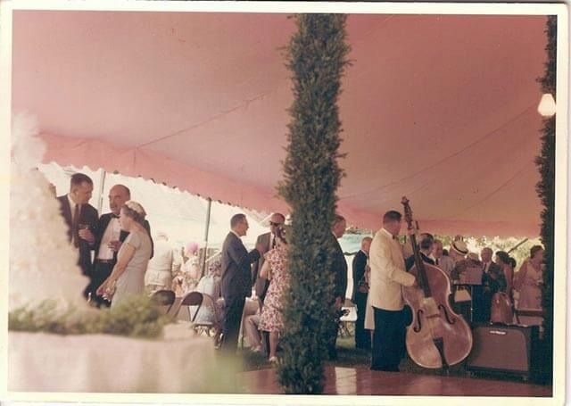 A group of people are standing under a tent with a man playing a double bass.