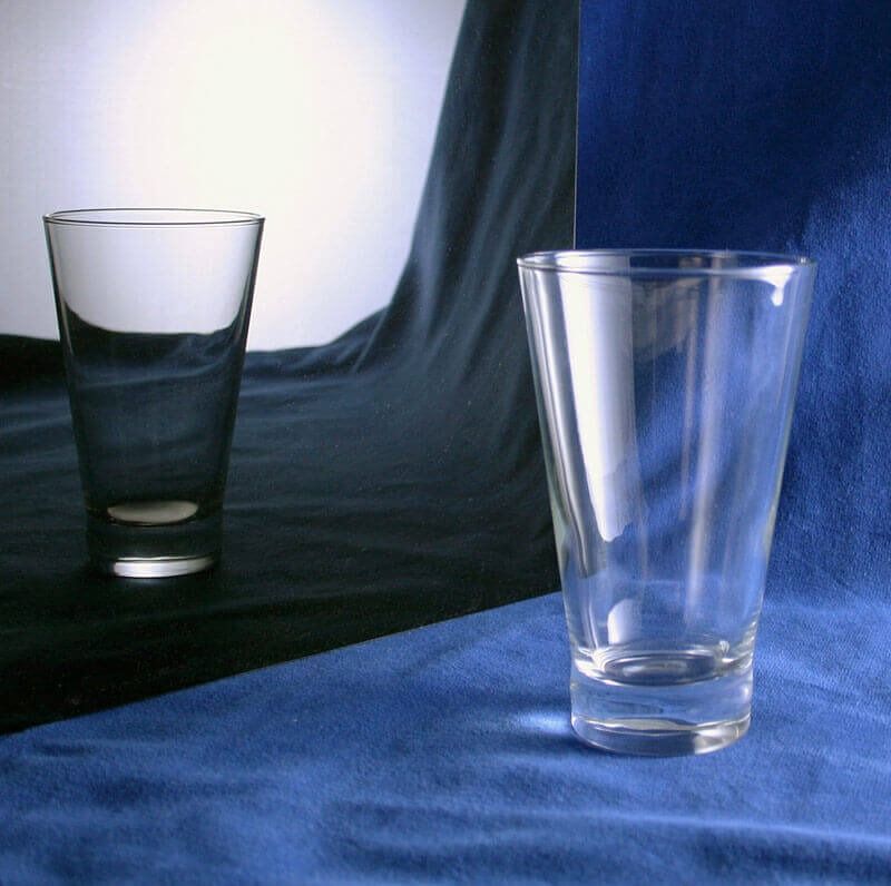 Two glasses are on a blue cloth and one is empty