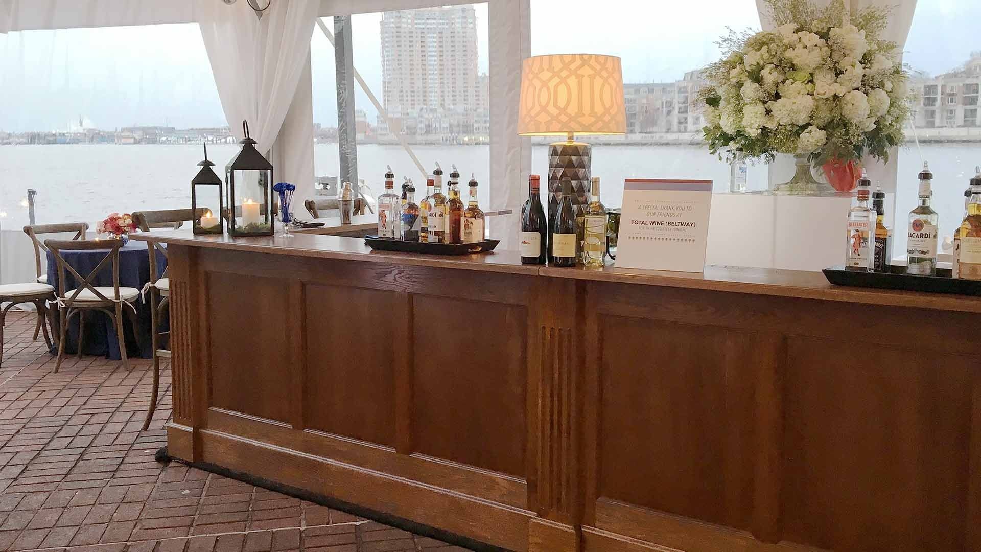A long wooden bar filled with bottles of liquor and flowers.