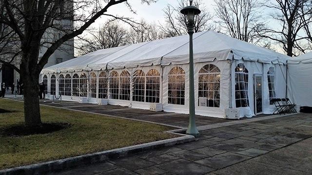 A large white tent with a lot of windows is in a park.