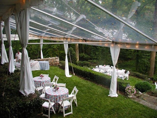 A clear tent with tables and chairs underneath it in a backyard.