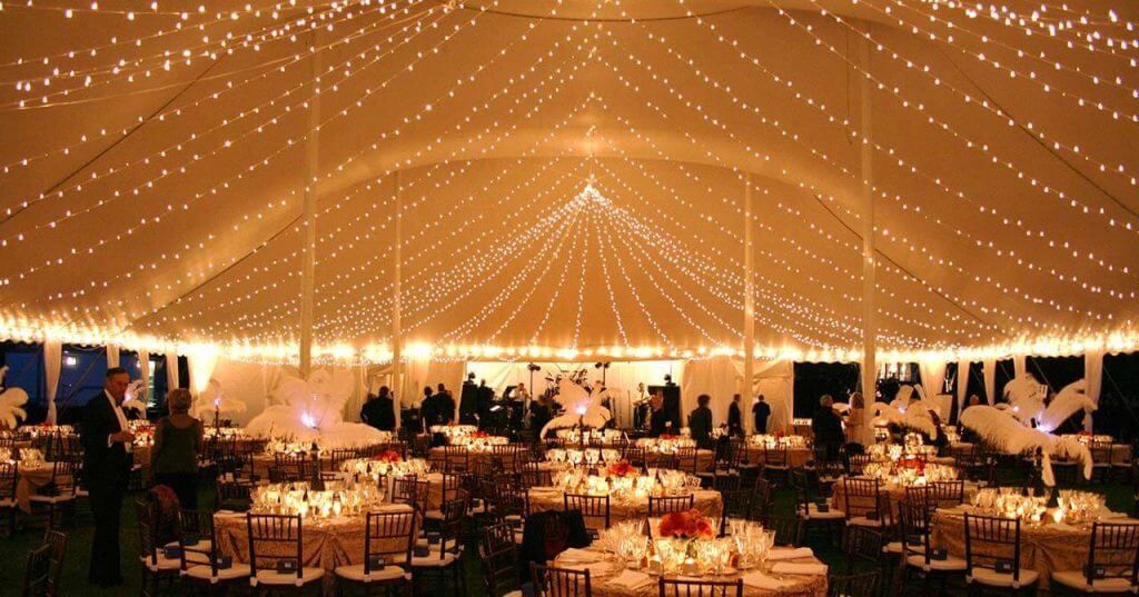 A large tent filled with tables and chairs with lights hanging from the ceiling