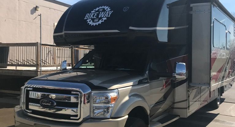 Tan and red RV parked in front of a building with the words 