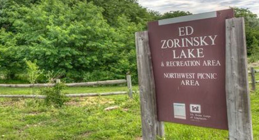 Sign for Ed Zorinsky Lake & Recreation Area, Northwest Picnic Area, brown and white sign in front of green trees and fence.