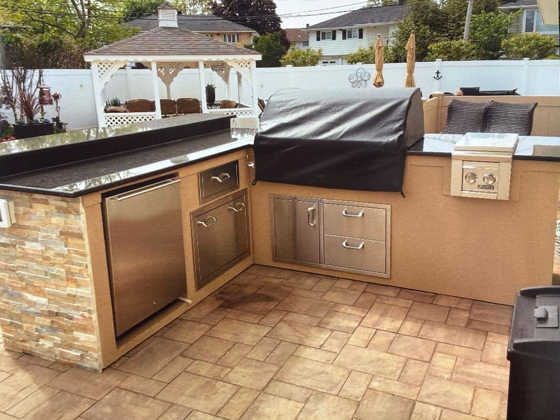 Outdoor kitchen with stainless steel appliances, stone accents, and covered grill.