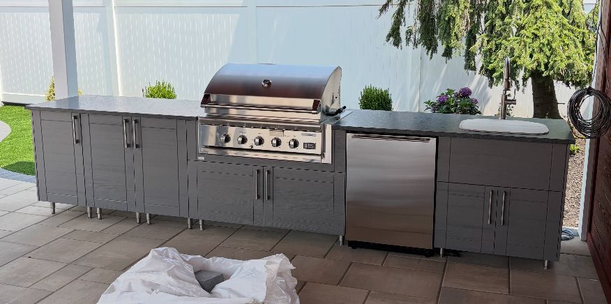 Outdoor kitchen with gray cabinets, stainless steel appliances, and a grill.