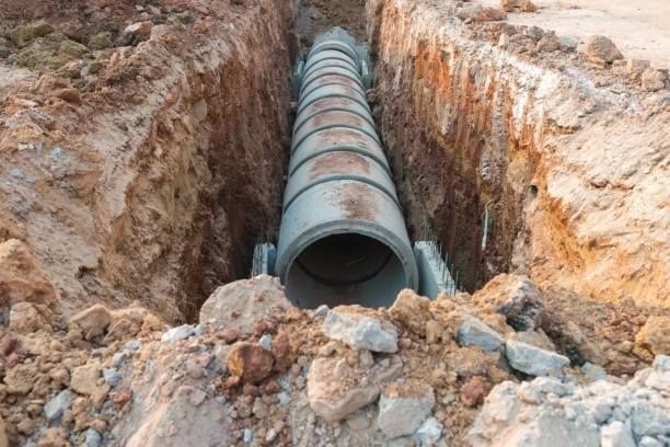 Large pipe sections laid in a deep dirt trench at a construction site
