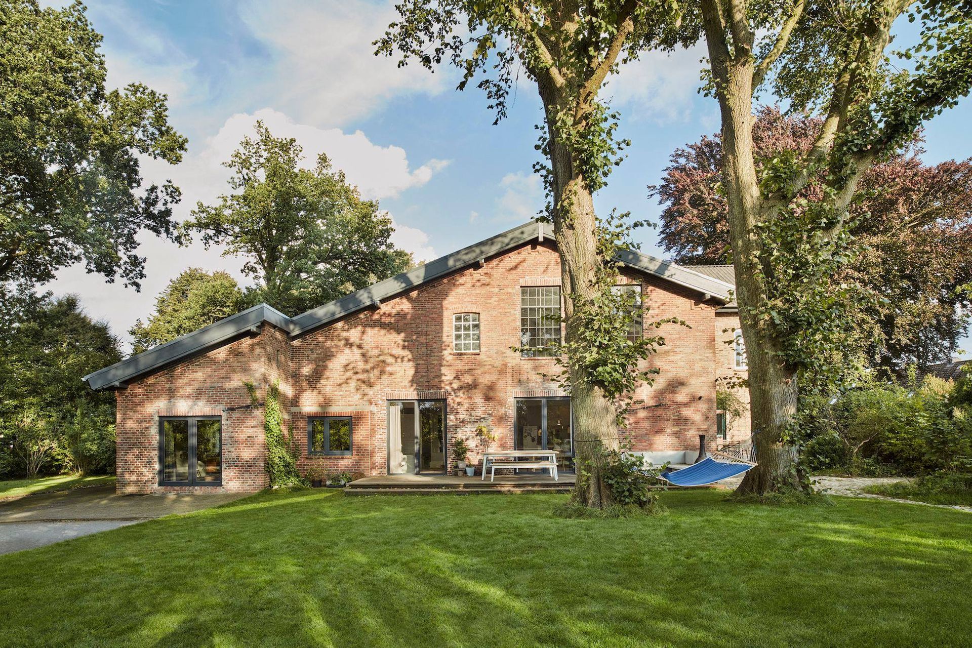 Brick house with a green lawn, tall trees, and a blue sky behind it