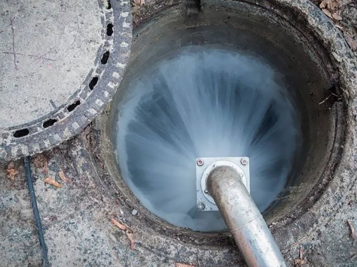 Water swirling down a circular drain with a metal pipe entering from the right.