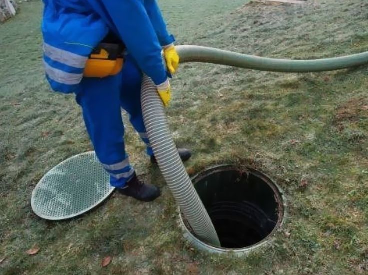 Worker in blue coveralls using a hose to clean a manhole opening outdoors