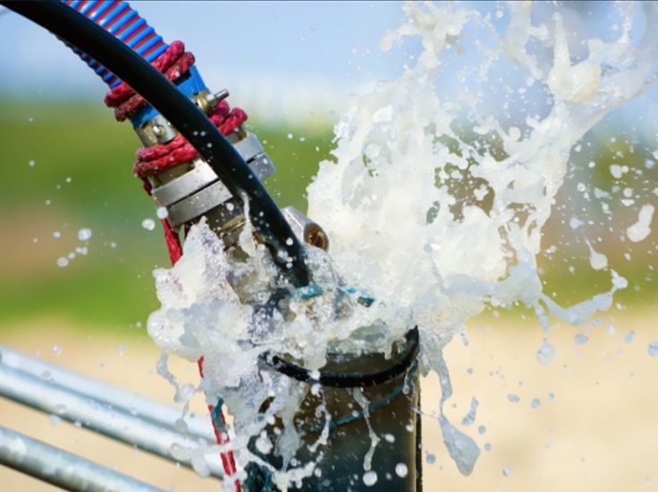 Water splashing from a garden hose nozzle with black and red hoses attached