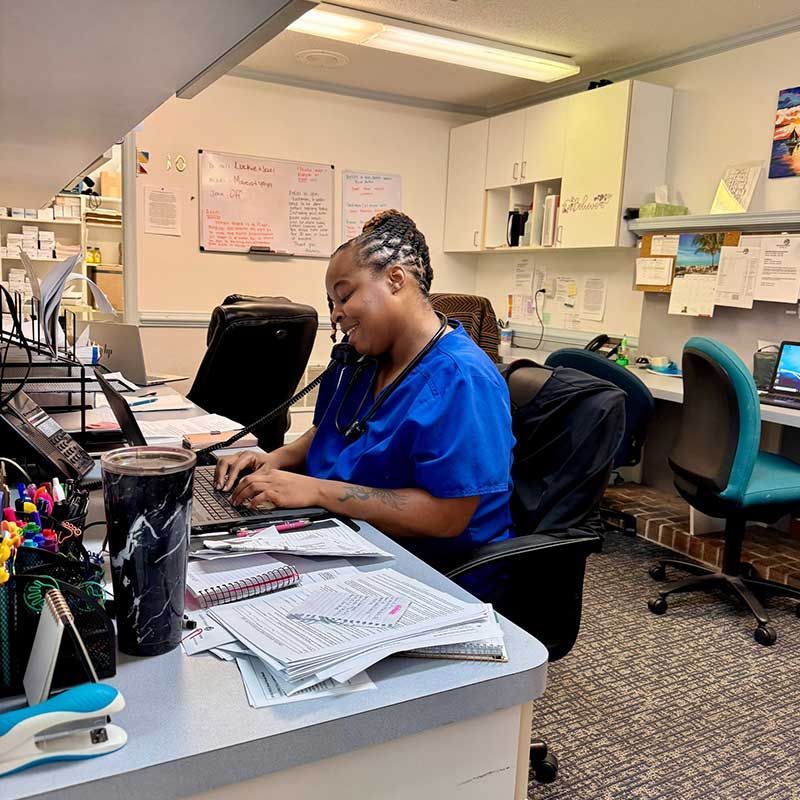 a woman in a blue scrub is sitting at a desk using a laptop computer