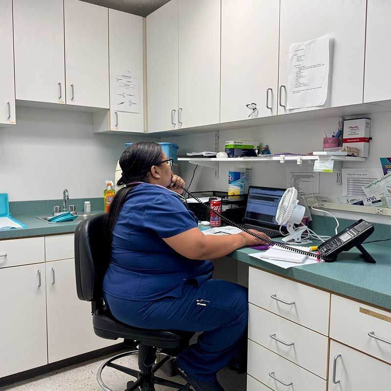 a nurse is sitting at a desk using a phone and a laptop computer