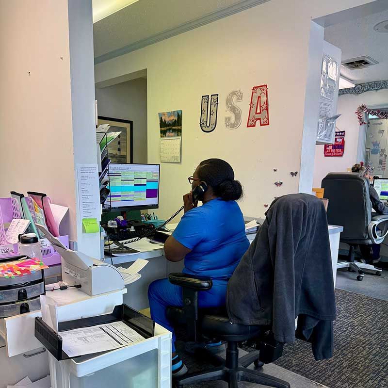 a woman in scrubs is sitting at a desk talking on a phone