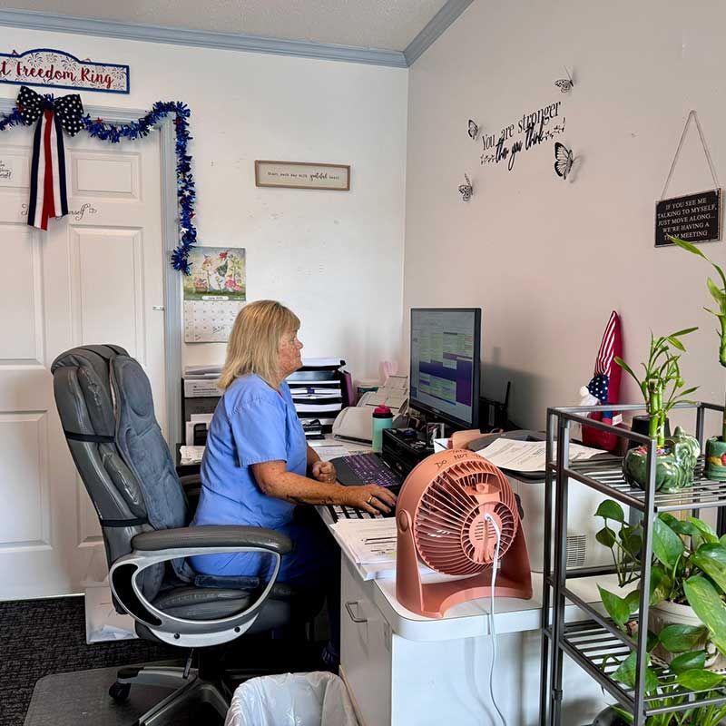 a woman sitting at a desk with a computer and a fan