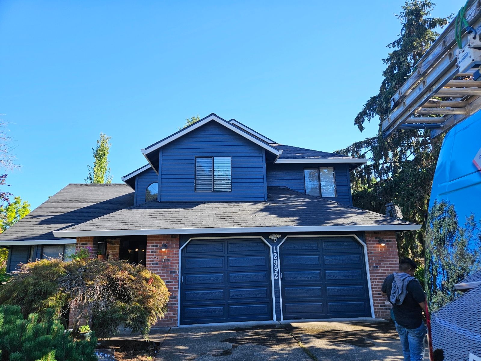 A man is standing in front of a house with a blue van parked in front of it.