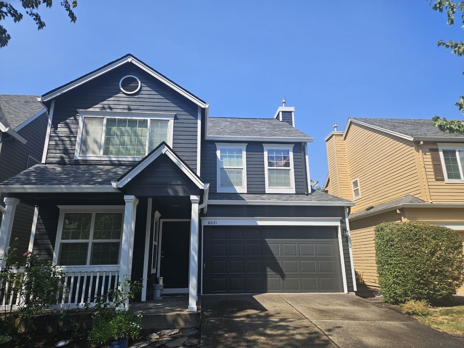 A black house with a white porch and a black garage door.