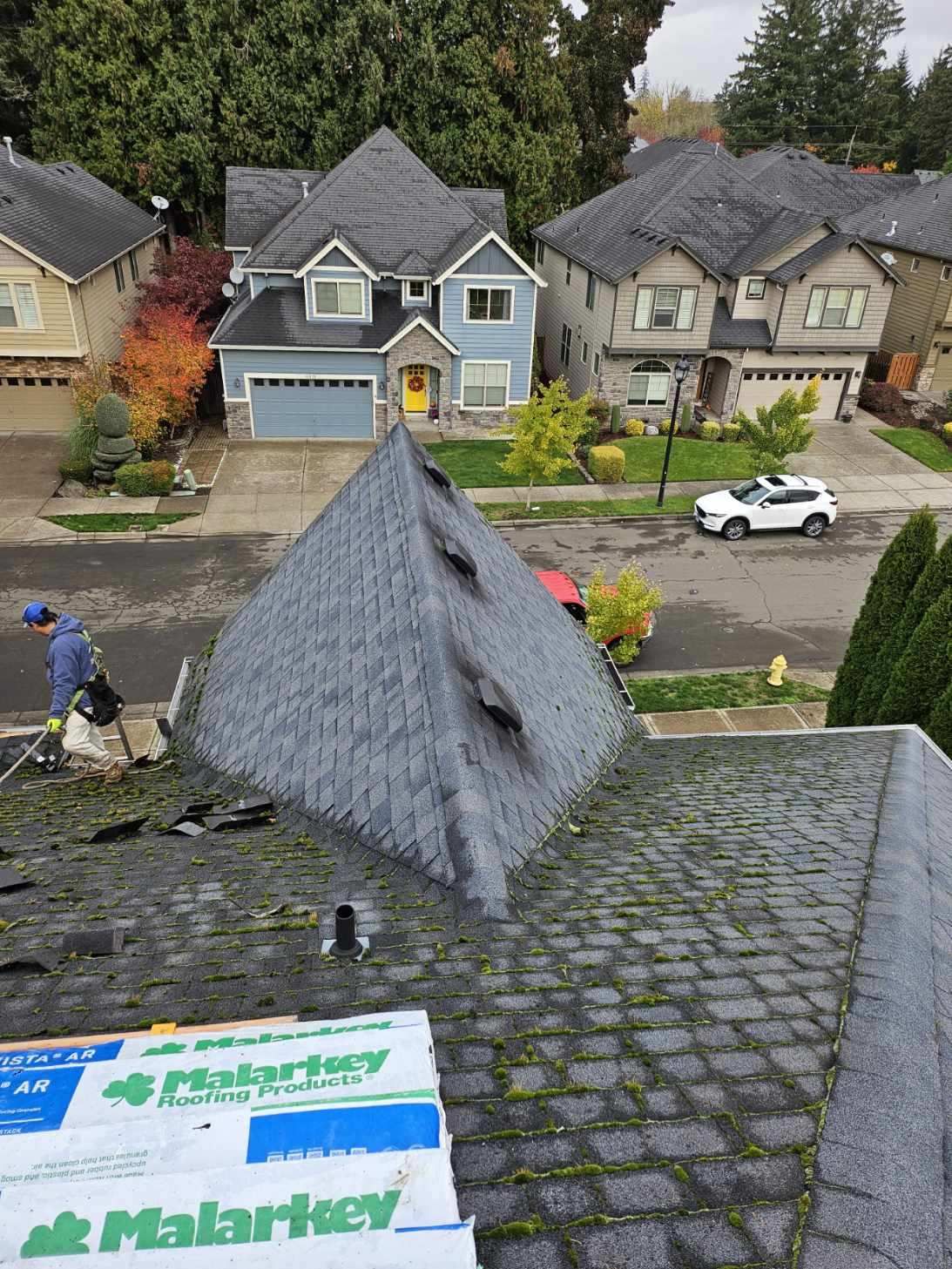 A man is working on the roof of a house in a residential area.