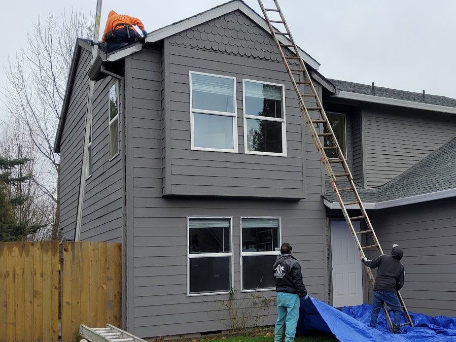 Two men are painting the side of a house with a blue tarp.