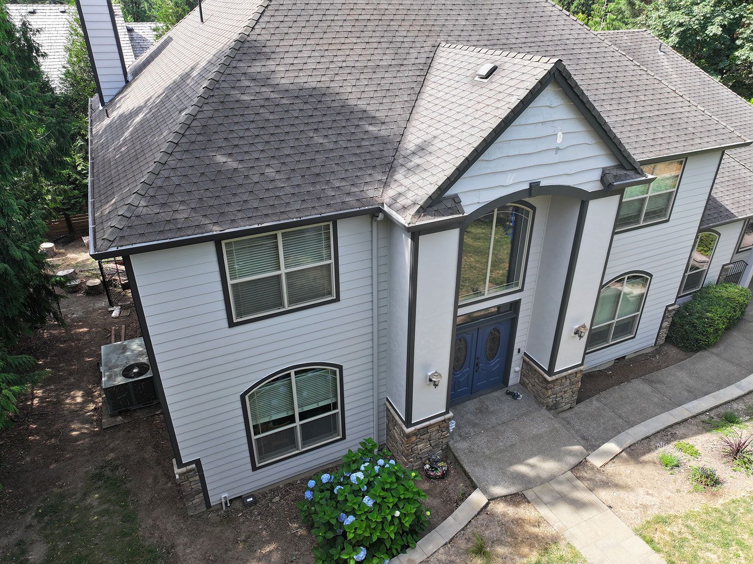 An aerial view of a large white house with a gray roof surrounded by trees