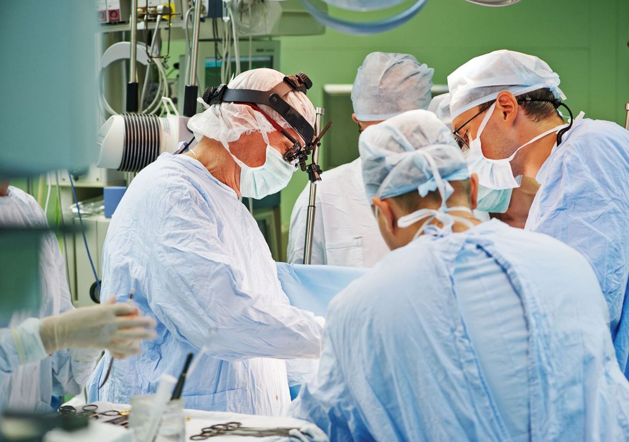 Surgeons in blue scrubs and masks perform an operation in a bright hospital operating room.