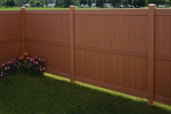 Backyard with a brown wooden fence, green lawn, and pink flowers in the corner