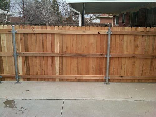 Wooden privacy fence with metal posts beside a concrete driveway in a residential yard
