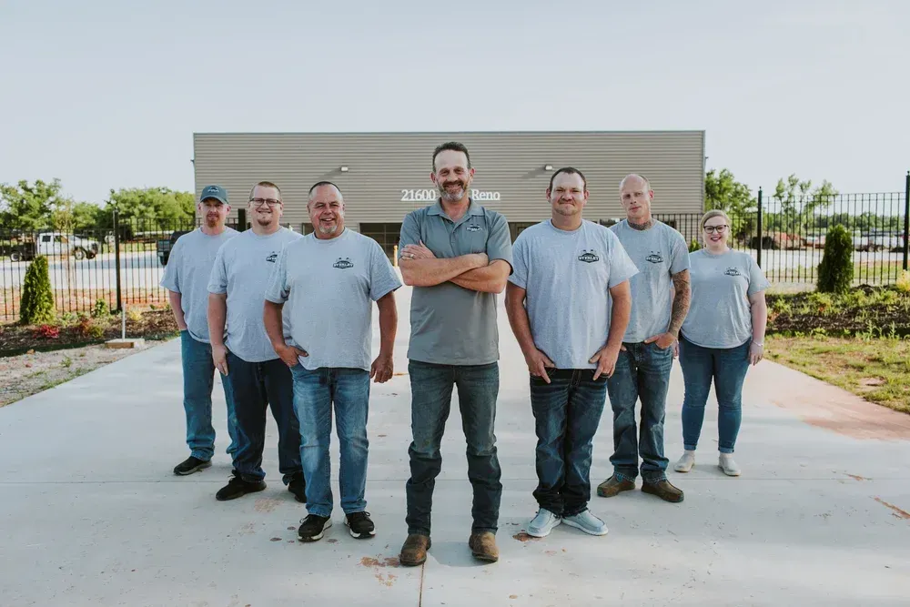Seven people standing in front of a building, with one person centered and arms crossed.